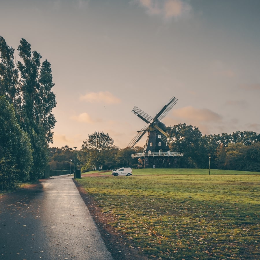 A car is parked next to a windmill in a park.