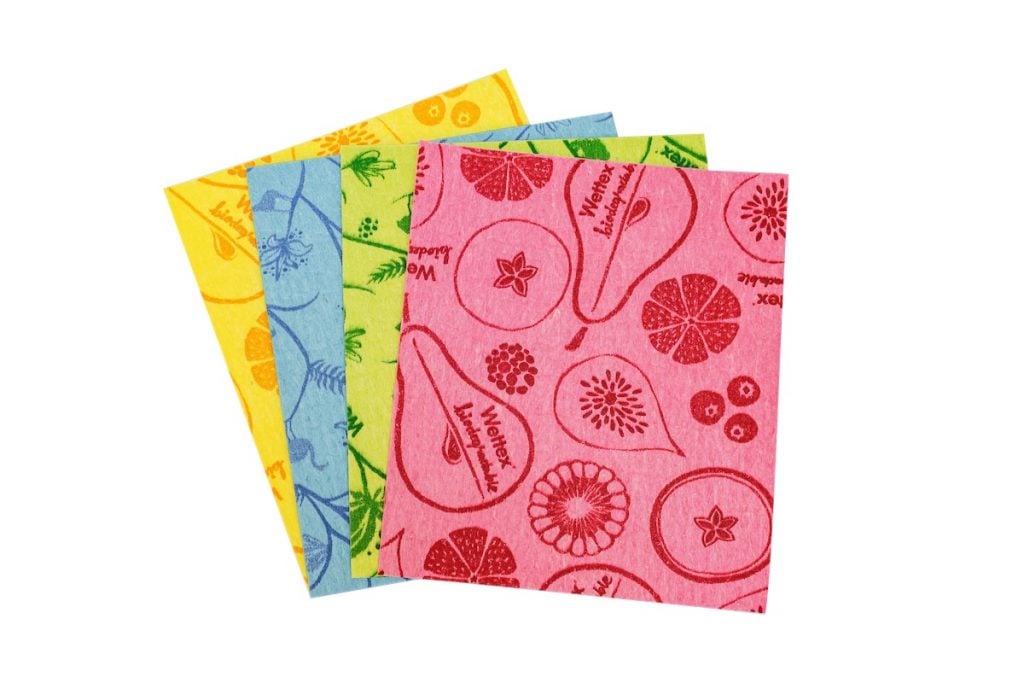 Four colorful cleaning cloths are laid out on a white background. Each cloth features a different food-themed design: yellow with lemons, green with herbs, blue with vegetables, and pink with fruits.