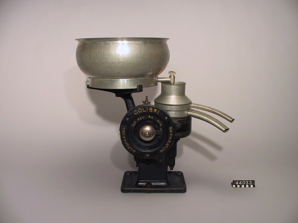 A metal cream separator with a large bowl on top, black metal base, and two spouts extending from the right side. A small label with the number 44033 is placed in front of the machine.