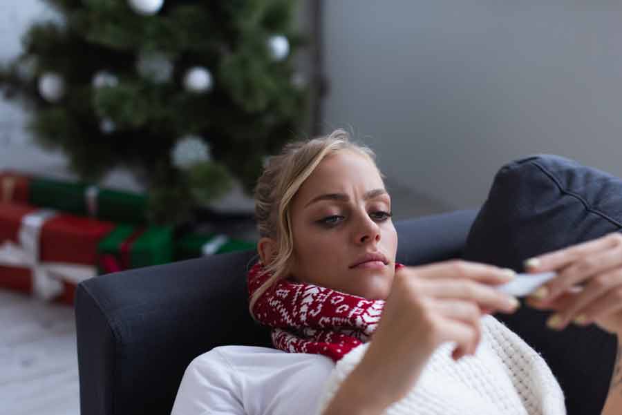 A woman is sitting on a couch with a christmas tree in front of her.